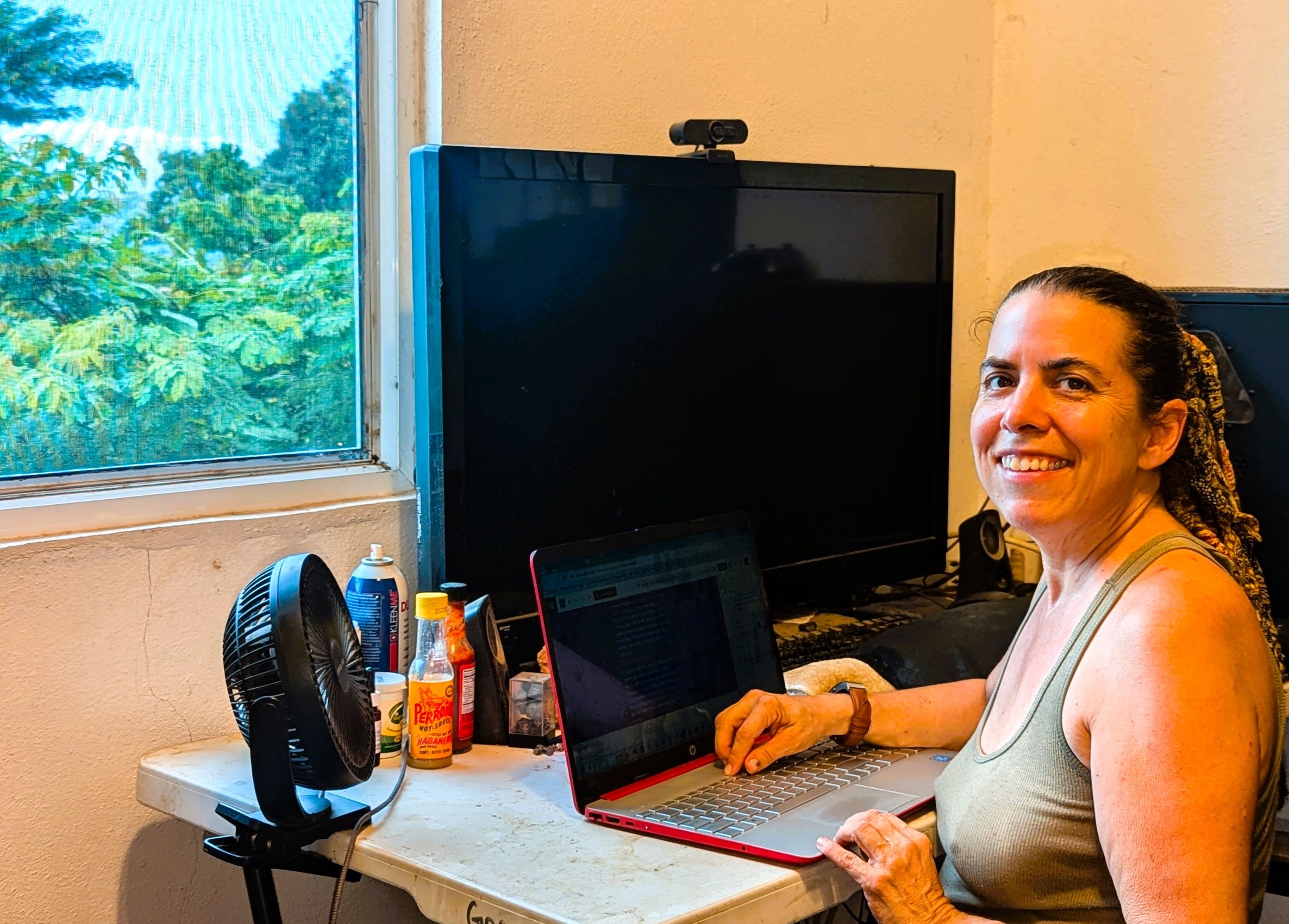 Julie smiling at her desk with an open laptop, in front of a window with a view of tropical plants.