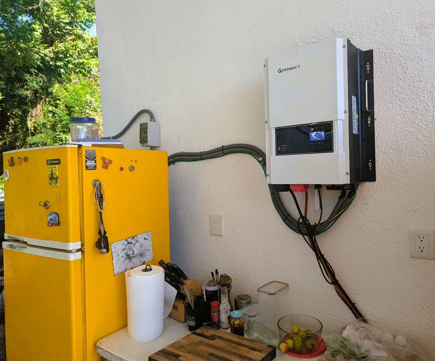 A white inverter mounted on the wall to the right of a yellow refrigerator.